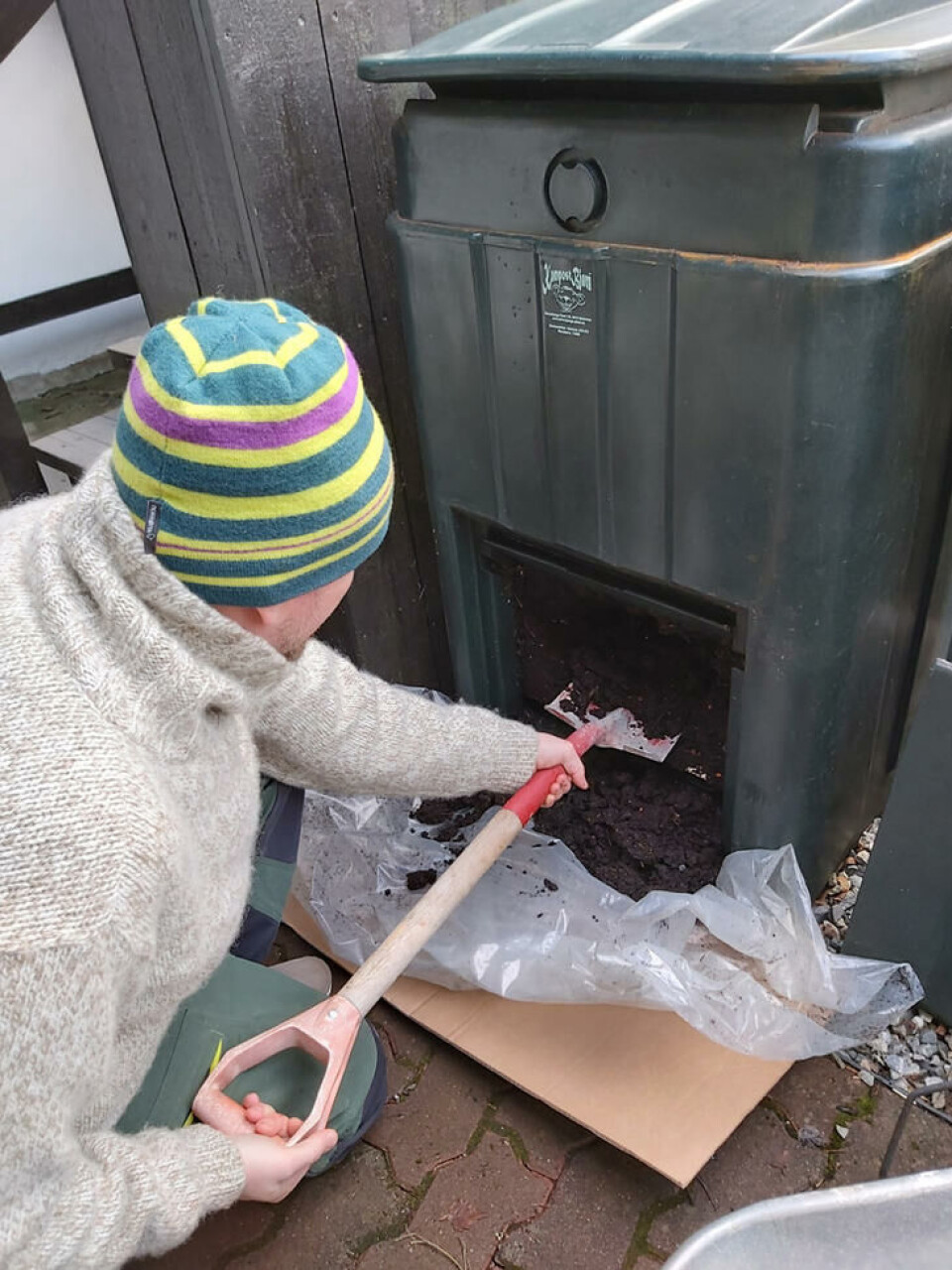 En varmkompostbeholder kan i løpet av ganske kort tid omdanne matavfall til deilig, mørk kompost. Foto: Marianne Utengen Mann tømmer jord fra varmkompostbinge med spade.
