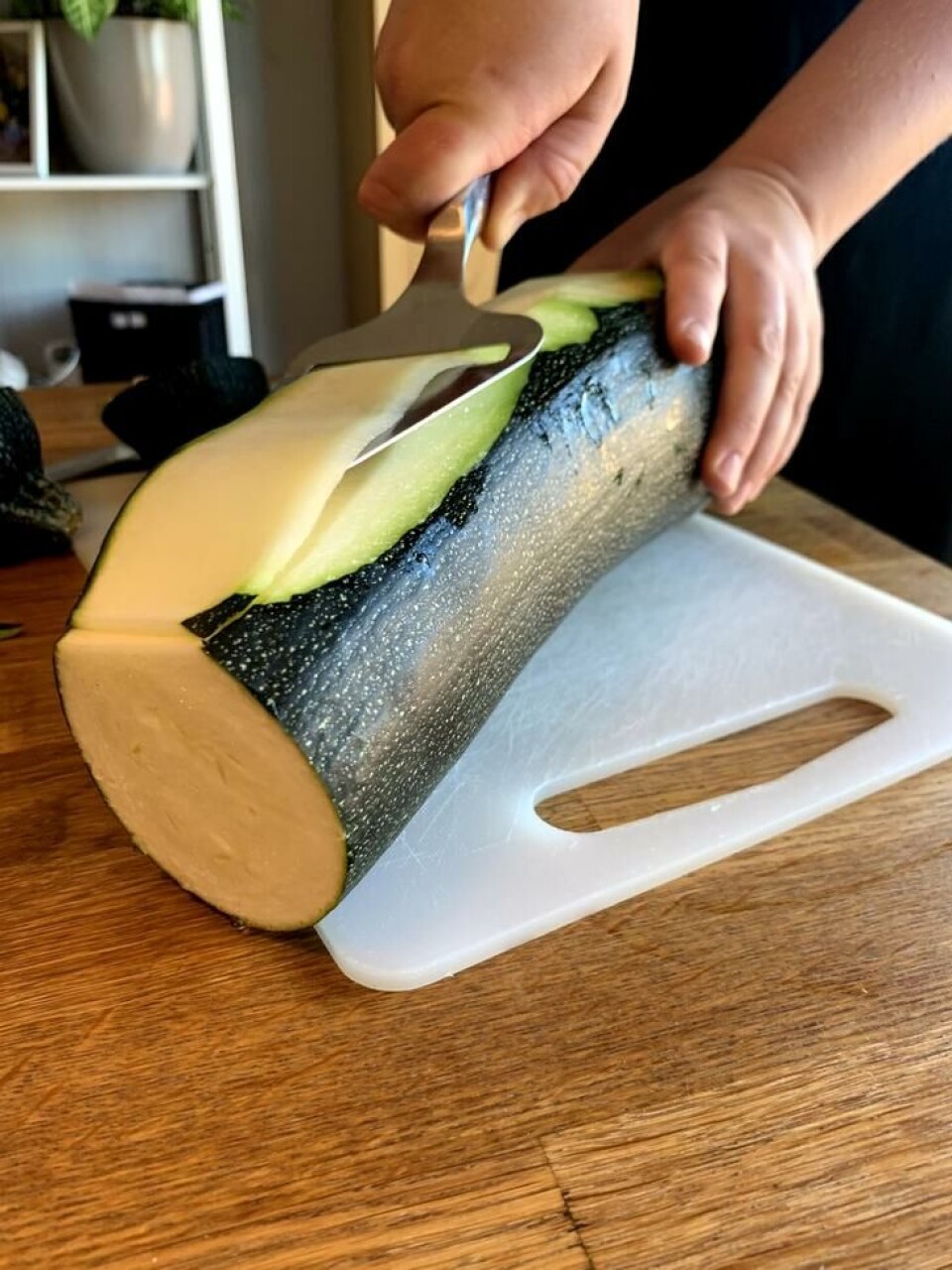 Ostehøvelen er grei å benytte når squashen skal høvles i tynne skiver. En hånd som skjærer en stor slash i skiver med ostehøvel.