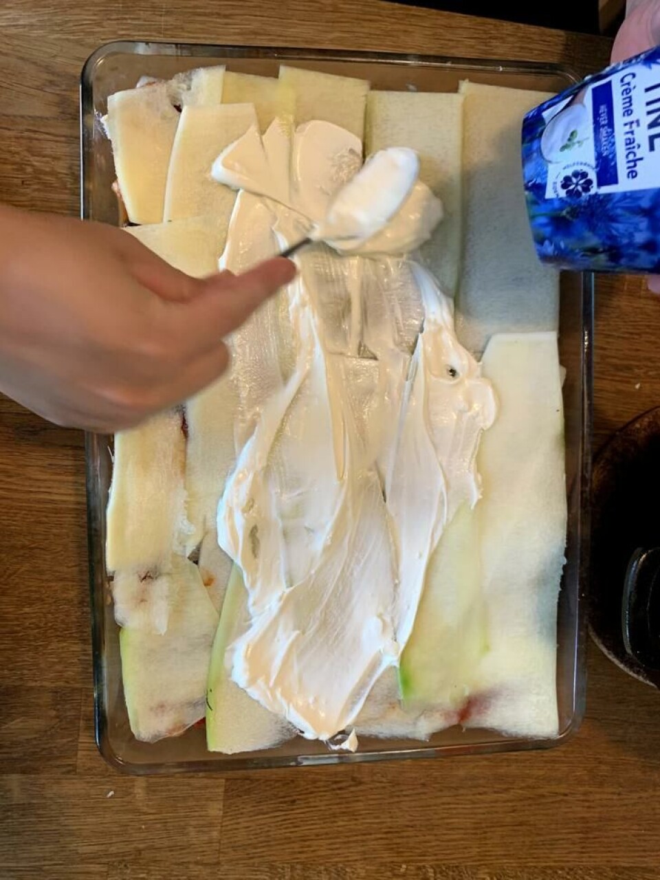 Så et lag med høvlet squash, med creme fraiche og fetaost smurt over. Forsett slik, lag på lag, til sausen er brukt opp. Avslutt med revet ost på toppen. Craime fraiche fordeles med skje utover et lag med squash-skiver.